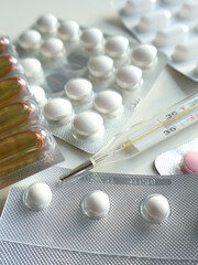 Blister packs containing white and colorful pills are arranged on table alongside a mercury thermometer, depicting healthcare and medication-related scene focusing on pharmaceuticals and cold remedies