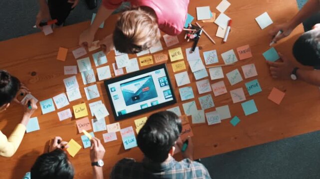 Top down view of programmer brainstorming and planning about web design while looking at tablet wireframe prototype. Aerial view of skilled developer team talking about digital application. Symposium.