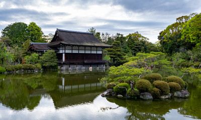 Obraz premium Heian Shrine and its gardens reflecting on the peaceful waters of a pond surrounded by lush vegetation, in Sakyo-ku, Kyoto, Japan.