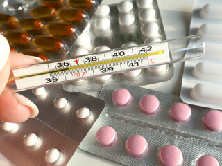 Various packaged medicines and thermometer showing marked temperature, depicting health care and medical concepts. Relevant for health management, pharmaceuticals, and temperature assessment imagery