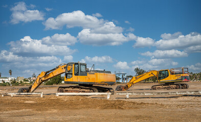 two excavators parked on a construction site in an residential area , daytime cloudy sky, sunny day