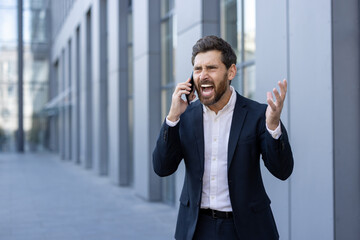 Businessman Expressing Anger During Phone Call Outside Modern Office Building