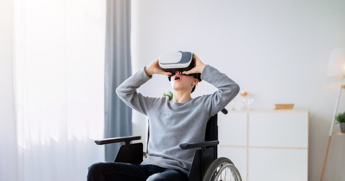 Happy handicapped teen boy in wheelchair using VR headset to explore augmented reality at home. Cheerful disabled teenager playing virtual online game, having fun with futuristic technologies indoors