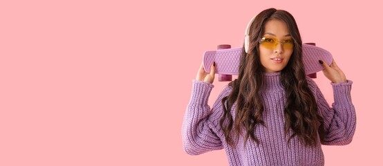 Young Asian woman in stylish sunglasses, with headphones and skateboard on pink background with space for text