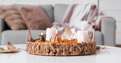 Wicker tray with glowing candles and autumn leaves on table in room