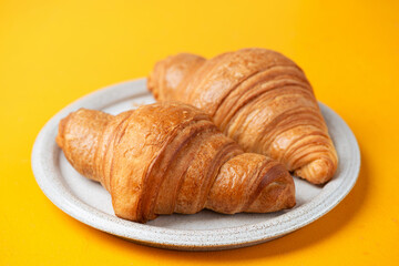 Two french croissants on a plate, yellow background