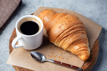 Cup of espresso black coffee and french croissant on wooden serving board