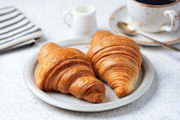 Two french croissants, marmalade, cup of coffee and coffee creamer in jug