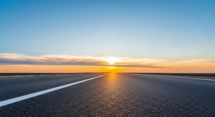 Empty asphalt road leading towards a bright sunset with a clear blue sky horizon