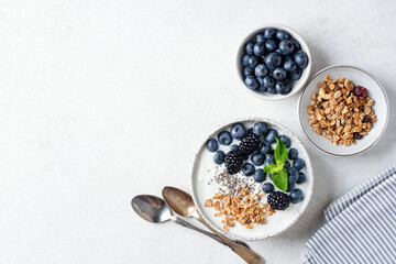 Muesli with yogurt, blueberries, blackberries and chia seeds. Top view on grey concrete table background, copy space