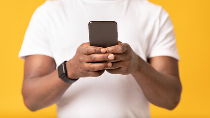 Modern technology, typing messages, modern chat and mobile applications. Adult african american guy in white t-shirt uses smartphone, isolated on orange background, studio shot, copy space, close up