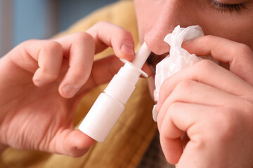 Ill young man with tissue using nasal drops at home, closeup
