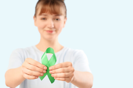 Young woman with green ribbon on light background, closeup. Glaucoma awareness month