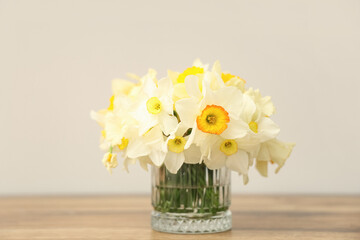 Glass vase with beautiful bouquet of daffodils on wooden table on light background, closeup