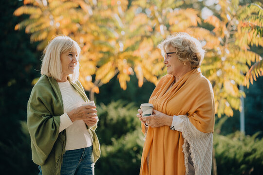 Two senior women enjoying coffee and conversation in autumn park