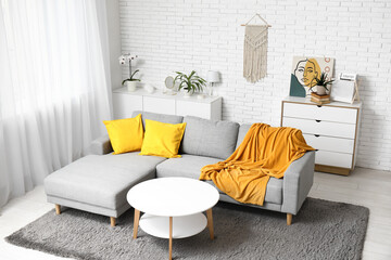 Interior of light living room with comfortable sofa, cushions and yellow plaid