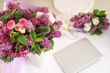 Vase with lilacs and laptop on table in flower studio