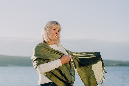 Smiling senior woman holding green shawl by the lake enjoying retirement