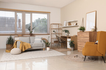 Interior of stylish living room with brown armchair, chest of drawers, workplace and comfortable sofa