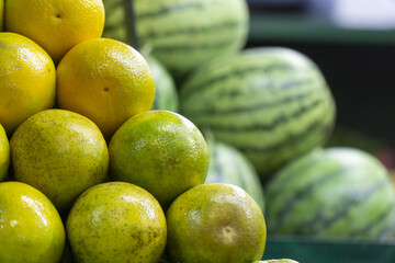 Fresh oranges stacked in front of striped watermelons at a fruit market