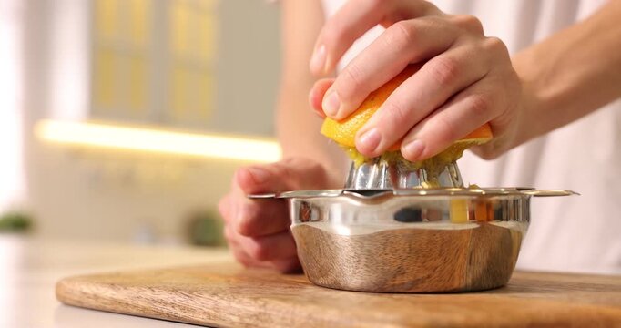 Making juice. Woman with orange using juicer at table indoors, closeup