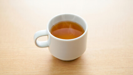 A cup of tea is placed on a wooden table in a bright setting