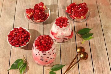 Glasses with pomegranate yogurt with pomegranate pieces, raisins with fresh cream for healthy eating. Healthy breakfast with ingredients, kitchen background, Natural nutrition and diet concept, menu