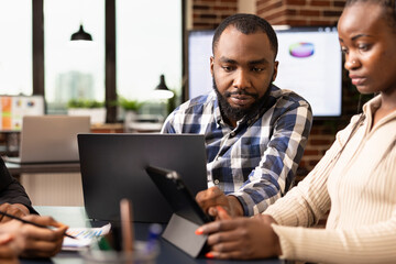 Closeup of black male manager with laptop, reviewing marketing strategy and plans of female employee in office. African american business professionals preparing and analyzing financial reports.