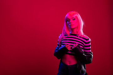 Beautiful woman in edgy fashion outfit exudes powerful elegance under cool pink tones, striking bold pose. Stylish female model stands dramatically beneath magenta lighting in modern studio.
