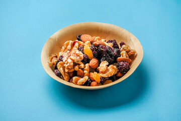 A bowl of nuts and dried fruit on a blue medical background. The bowl is made of wood and the food is colorful. Healthy diet add on. Eat natural food concept.