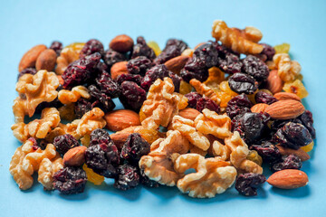 A blue background with a variety of nuts and dried fruit. The nuts include almonds, walnuts, and cashews. The dried fruit includes raisins and cranberries. Concept of abundance and variety and health