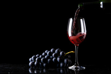 Red wine being poured into a glass next to dark grapes