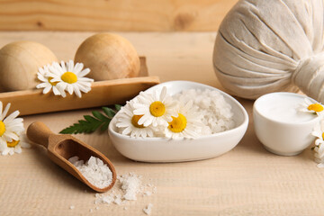 Composition with bowl of sea salt, chamomile flowers and massage balls on wooden background, closeup