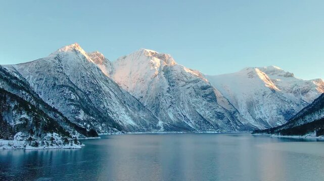 panoramic view of the snow capped mountains and serene waters of Eresfjord or the Eikesdalen region in Norway during winter, capturing the golden hour light on the peaks and the tranquil beauty of the