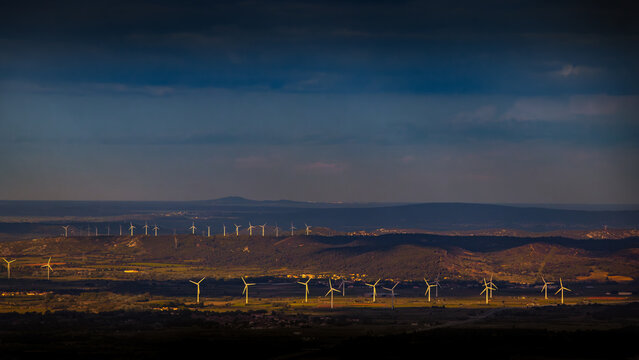 Wind turbines seen from the top of Mount Alaric in the Aude region. Landscapes interspersed with sunbeams sculpted by clouds in the south of France in Occitanie.