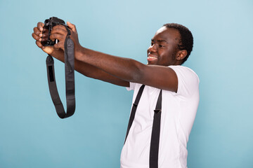 Black man with joyful expression takes a self portrait using his camera. Male photographer in...