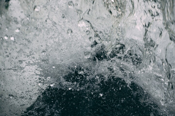 Close-up of water crashing onto a rock, capturing suspended droplets and dynamic motion in a dramatic, textured scene.