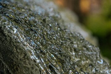 Close-up of water cascading downward, capturing crisp droplets and fluid textures against a soft green background.