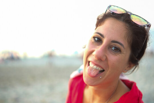 Beautiful brunette woman sticks out her tongue against the backdrop of a Sicilian beach. The woman is thirty-eight years old and of Caucasian origin from the Mediterranean area