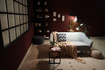 Interior of dark living room with grey sofa, table and glowing lamps at night