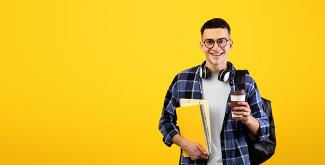 Happy male student with notebooks, backpack and takeaway coffee looking at camera and smiling on orange studio background. Cheerful young guy participating in educational program