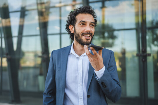 Smiling businessman using voice assistant on smart phone outdoors