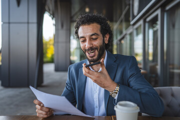 Businessman recording voice message while reading documents at outdoor cafe