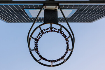 Outdoor basketball hoop with rusty metal chain net on a street playground against clear blue sky, urban sport and recreation concept