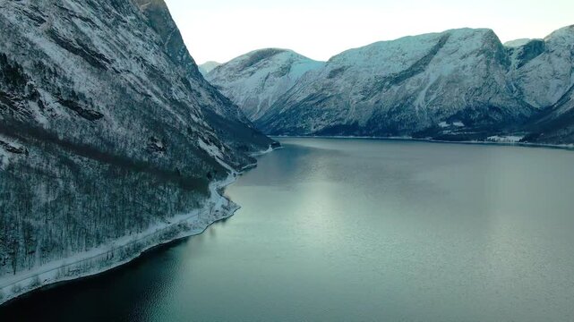 aerial view of a serene Norwegian fjord in winter, surrounded by snow dusted mountains and tranquil waters reflecting the overcast sky.