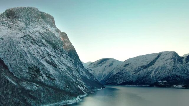 panoramic view of a tranquil Norwegian fjord in winter, with majestic snow-covered mountains reflecting in the calm, icy waters.