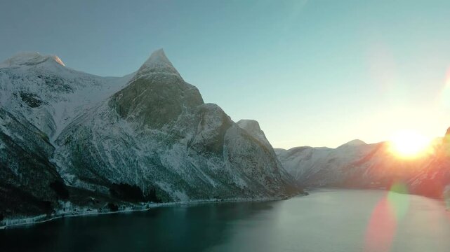 aerial footage capturing the stunning winter landscape of a Norwegian fjord, possibly Eresfjord or Eikesdalen, during a beautiful sunrise or sunset.
