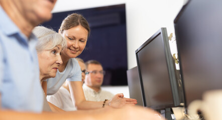 Concerned old woman sitting at computer while trainer explaining him something during IT courses