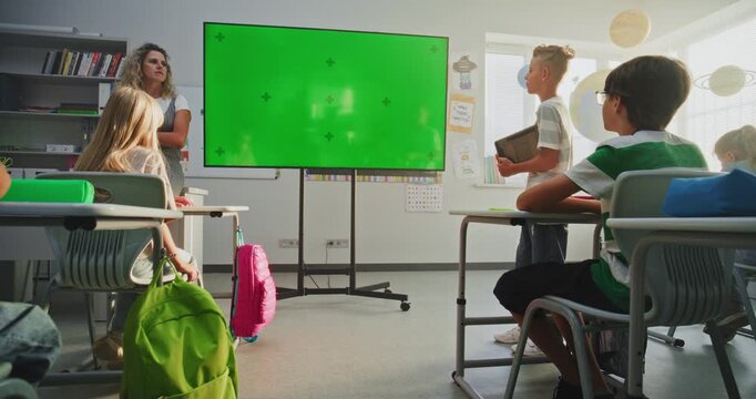 Elementary School Boy with Tablet Computer Giving Presentation in Front of Classmates and Teacher Using Large Digital Screen with Chroma Key Mock Up. Green Screen Template for Educational Content.