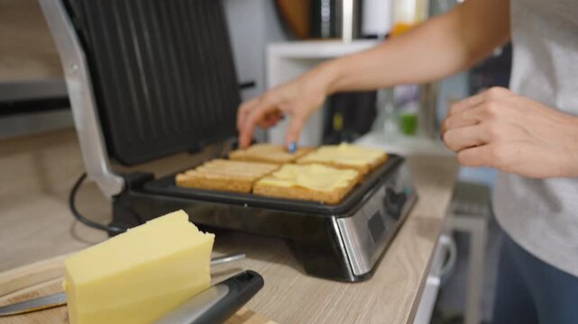 Hands Placing Cheese Slices on Toasted Bread on Electric Grill for Sandwich, close-up angle, Fast Food Concept